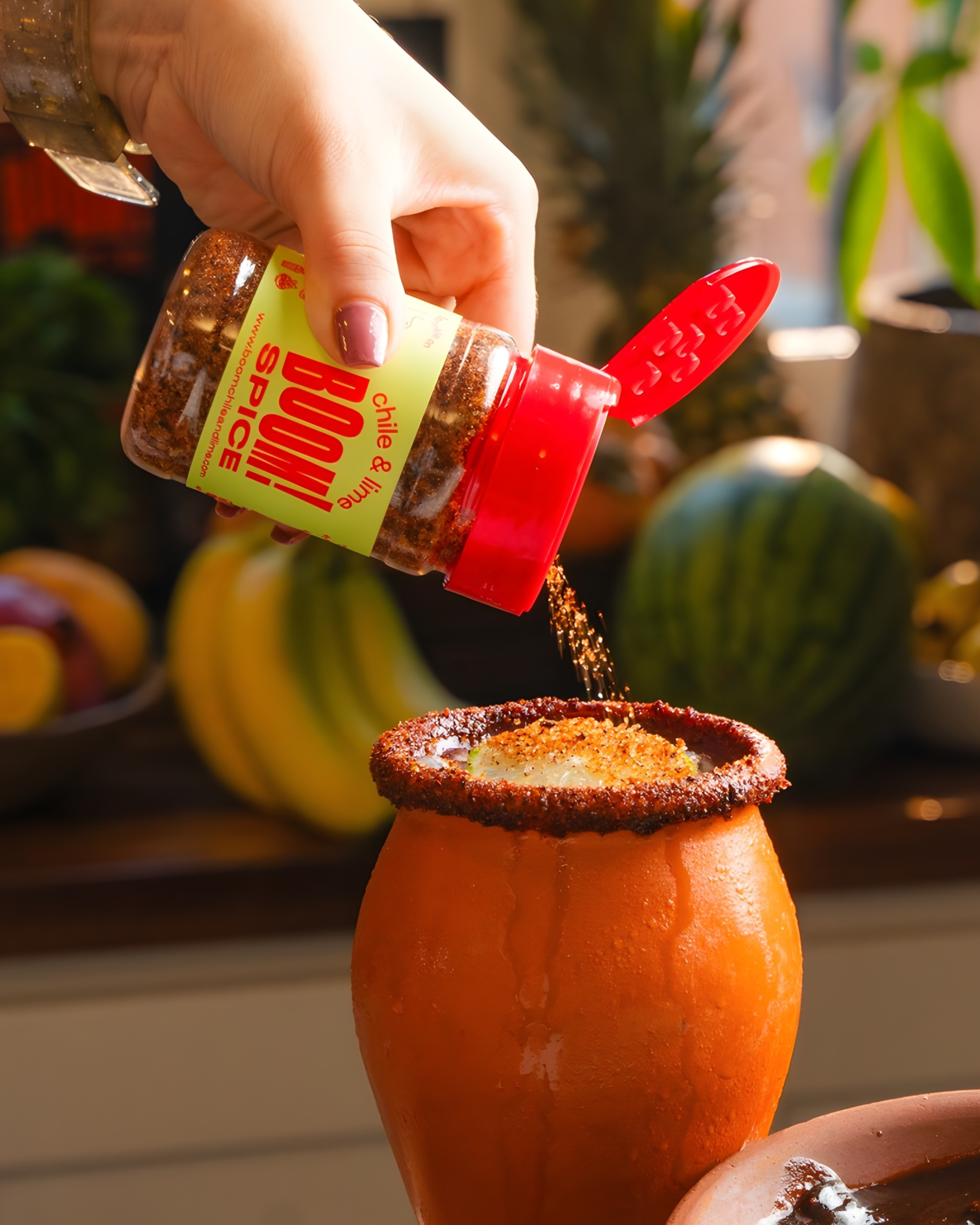 Hand sprinkling spice from a red and yellow container onto a cocktail in a pumpkin glass.