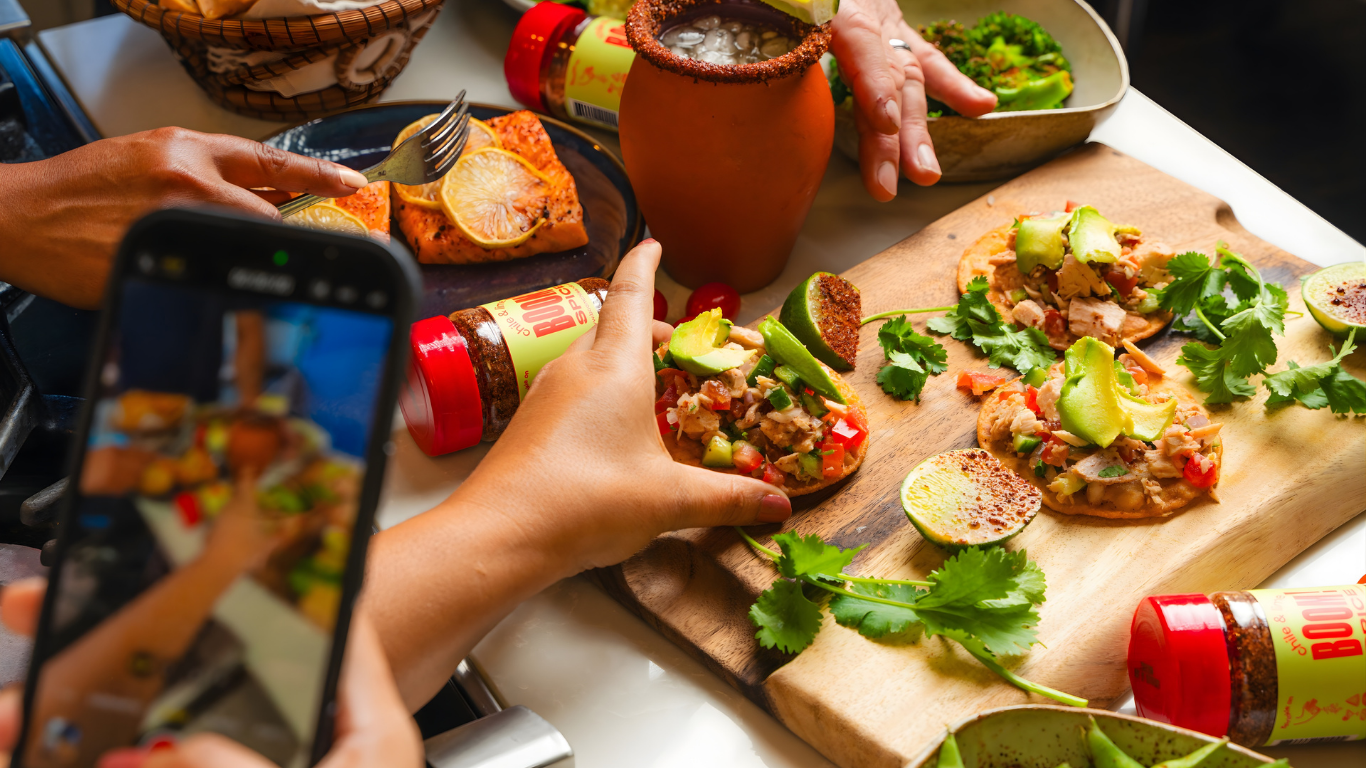 People preparing and taking photos of a meal on a wooden board with various ingredients.
