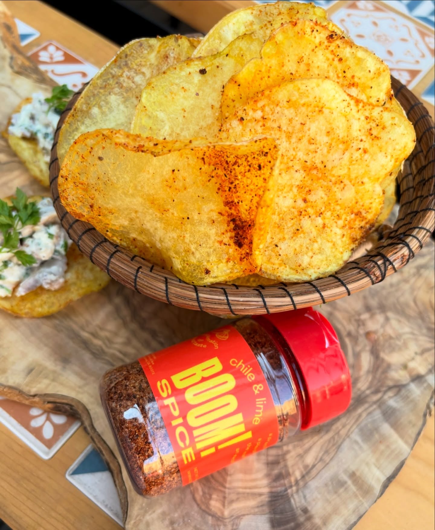 Basket of spicy potato chips with a bottle of BOOM! Spice on a wooden surface